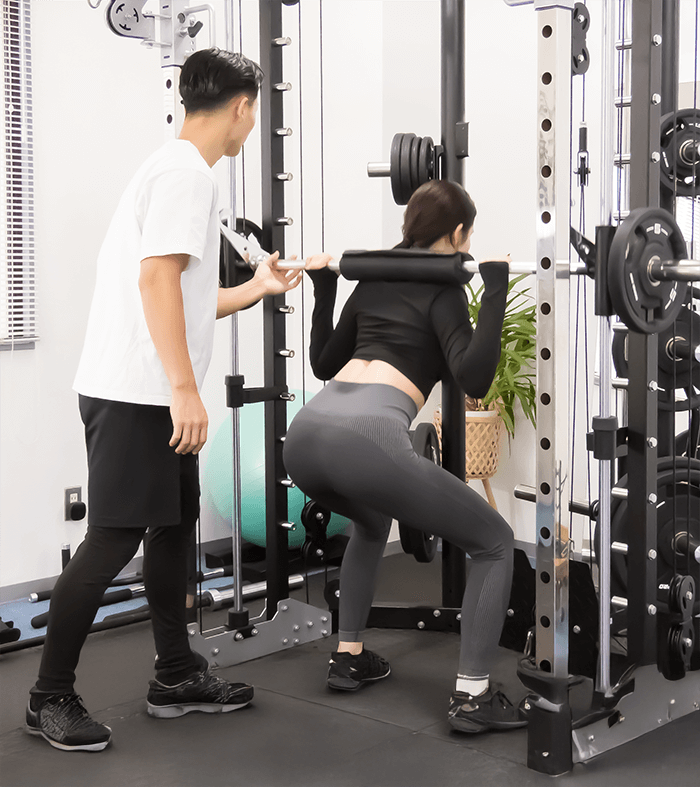 男性トレーナーに指導されてトレーニングをしている女性の画像
